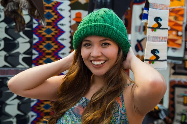 Nahaufnahme einer schönen lächelnden jungen Frau, die andine traditionelle Bekleidungstextilien berührt und von Hand in Wolle gewebt, farbenfroher Stoffhintergrund — Stockfoto