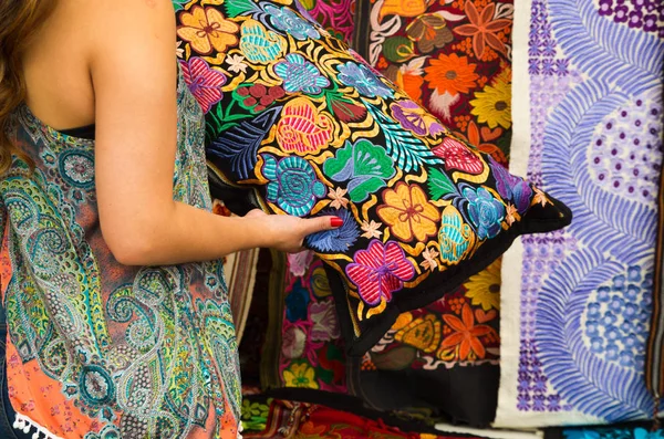 Acercamiento de una joven mujer sosteniendo en sus manos una almohada con flores coloridas afuera, ropa tradicional andina, telas coloridas de fondo — Foto de Stock