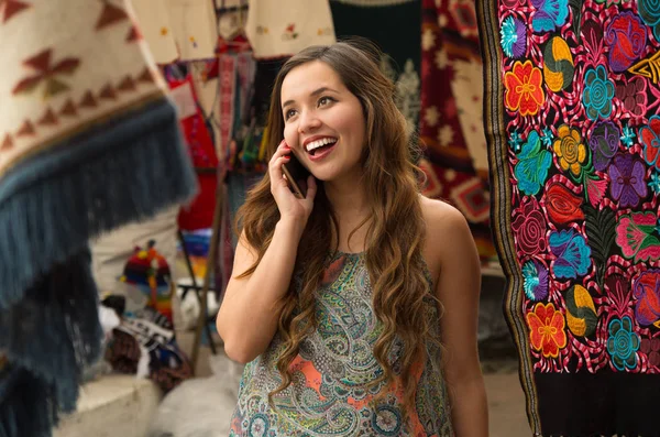 Mulher bonita sorrindo jovem usando seu celular, andino tradicional roupas têxteis fios e tecidos à mão em lã, fundo tecidos coloridos — Fotografia de Stock