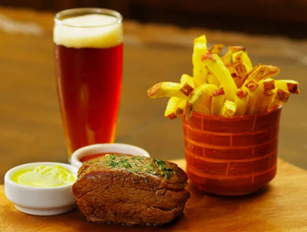 Delicioso filete de ternera con salsa de tomate, papas fritas y un vaso de cerveza sobre tabla de madera —  Fotos de Stock