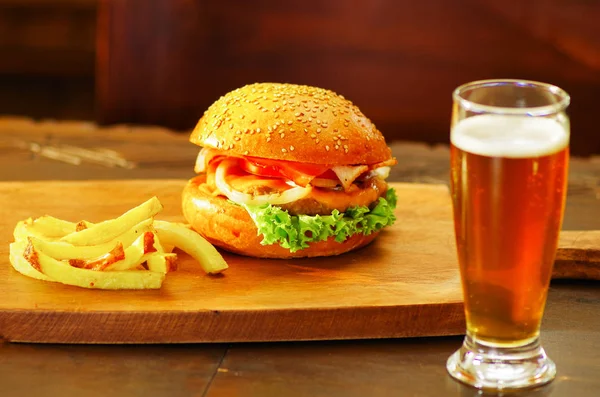 Deliciosa hamburguesa con carne de res, cebolla, tomate, lechuga y queso con papas fritas y un vaso de cerveza sobre tabla de madera —  Fotos de Stock