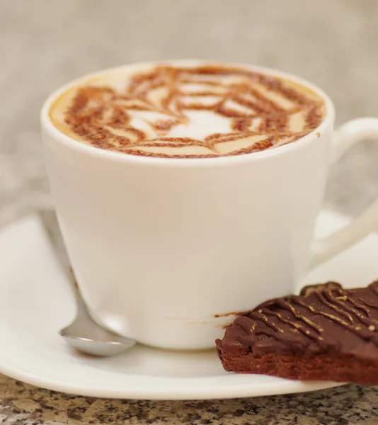 Närbild på en porslin vit kopp kaffe med blommönster med en brownie — Stockfoto