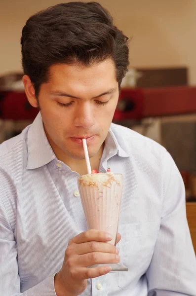 Красавчик пьет молочный коктейль с пластиковой соломинкой. — стоковое фото