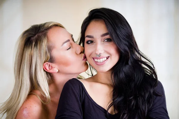 Primer plano de una sexy lesbianas amantes en una habitación por la mañana, rubia besando a una chica rubia en su mejilla, en un fondo blanco — Foto de Stock