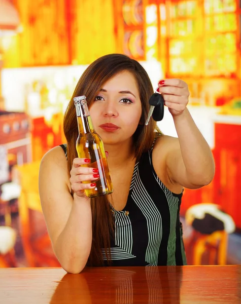 Portrait of a drunk woman holding a beer with one hand and her car keys with her other hand, in bar background — Stock Photo, Image