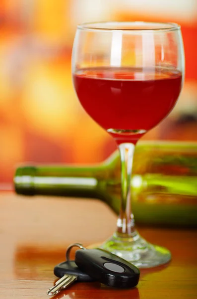 Close up of a cup of red wine with car keys on wooden tablea with a blurred green botle of wine behind — Stock Photo, Image