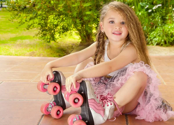 Menina pré-escolar sentada no chão tocando seus patins, em um fundo de jardim — Fotografia de Stock