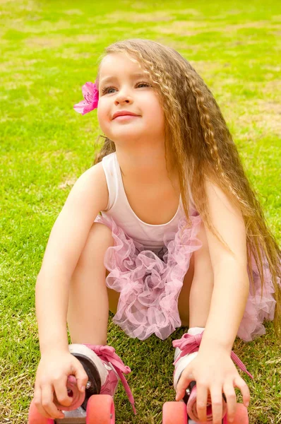 Petite fille maternelle débutant assis dans l'herbe avec ses patins à roulettes, dans un fond d'herbe — Photo