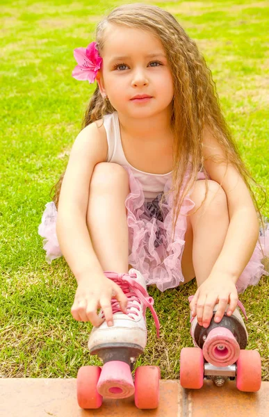 Little girl preschool beginner touching her roller skates, in a grass background — Stock Photo, Image