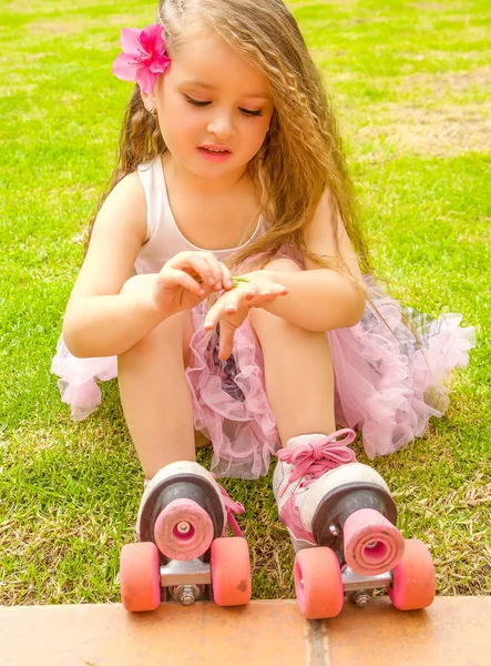 Little girl preschool beginner in roller skates, putting some grass in her hand, grass background — Stock Photo, Image