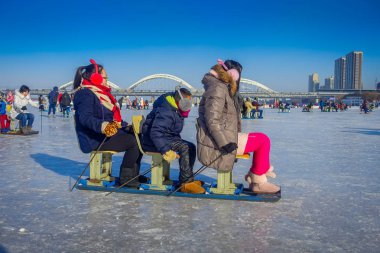 Harbin, China - February 9, 2017: Friends on a sled having fun on frozen river Songhua during winter time. clipart