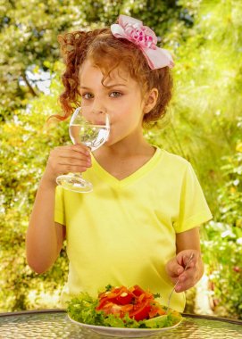 Bir bardak su içme ve Bahçe arka planda sağlıklı bir salata yemeye hazırlanıyor sarı bir tişört giyen güzel genç kız