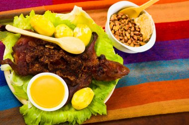 Traditional ecuadorian dish, grilled guinea pig spread out onto green plate, potatoes, tostados and lemons on the side, seen from above clipart