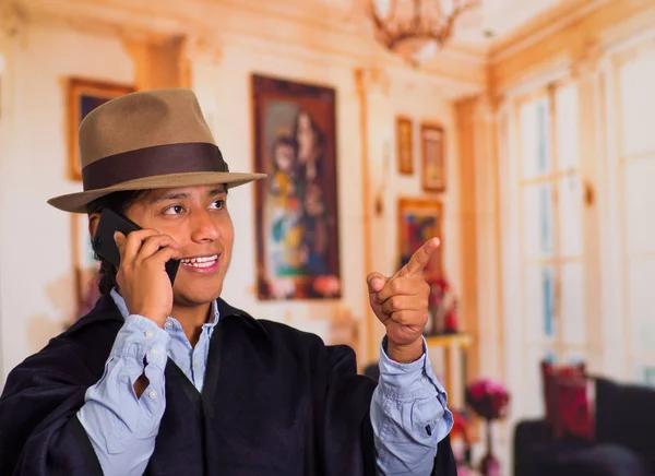 Közelről visel kalapot és használ sejt telefon poncsó őshonos fiatalember portréja — Stock Fotó