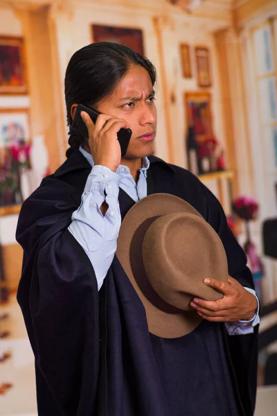 Närbild porträtt av ung inhemska man bära hatt och poncho med hjälp av mobiltelefon — Stockfoto