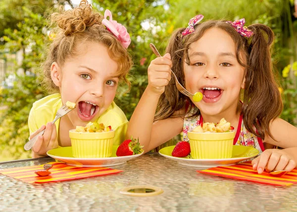 Two beautiful young girls, eating a healthy pineaple and grapes using a fork, in a garden background — Stock Photo, Image