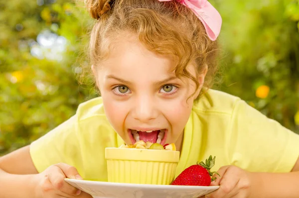 Close up of a beautiful young girl wearing a yellow t-shirt, preparing to eat a healthy fruit salad in a garden background — Stock Photo, Image