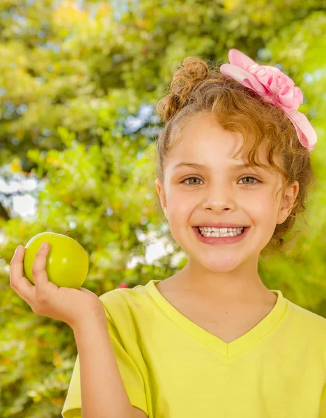 Mooi jong meisje, met een geel t-shirt houden van een gezonde appel, in een tuin achtergrond — Stockfoto