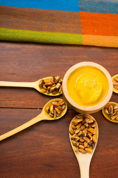 Wooden spoons with toasted corn grains, known as tostado in south america, spread around bowl containing yellow salsa, seen from above — Stock Photo, Image