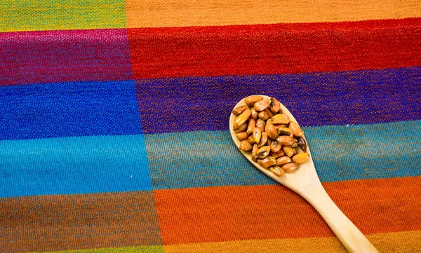 Cucharas de madera con granos de maíz tostados, conocidos como tostado en América del Sur, se extienden alrededor de un tazón que contiene salsa amarilla, vista desde arriba — Foto de Stock