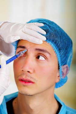 Yakışıklı bir genç adam, yüz estetik tedavi enjeksiyonları, doktorlar el şırınga tutarak ve tıbbi bir şapka eldiven ile alma closeup