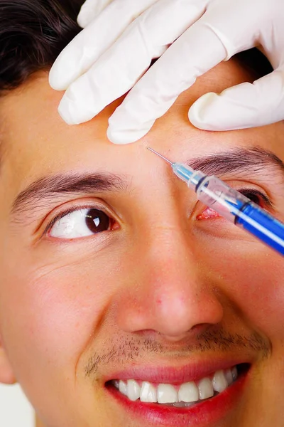 Primer plano de un joven guapo sonriente, recibiendo inyecciones de tratamiento cosmético facial, manos de médicos con jeringa de sujeción de guantes —  Fotos de Stock