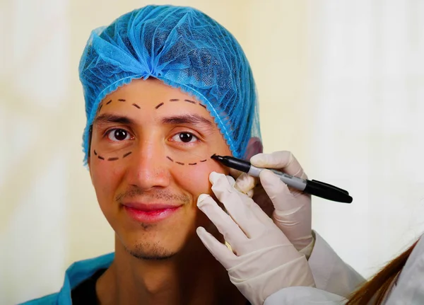 Surgeon drawing marks on male face. Plastic surgery concept