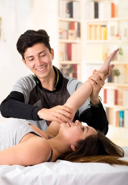 Sports massage. Hnadsome massage therapist massaging arms of a female athlete, in a doctor office background — Stock Photo, Image