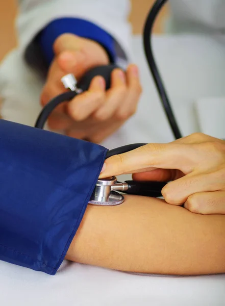 Nahaufnahme eines jungen Arztes mit dem Stethoskop, um den Puls zu hören, während eine Frau mit einem Tensiometer im Arm in einem Arztsprechzimmer sitzt — Stockfoto