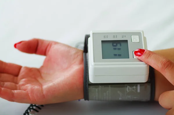 Primer plano de una paciente joven utilizando un tensiómetro automático en su brazo, en un fondo de consulta médica —  Fotos de Stock