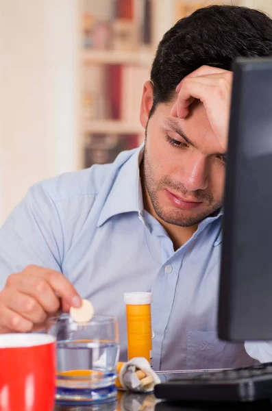 Bonito homem entediado caindo uma pílula comprimido efervescente em um copo de água em seu escritório — Fotografia de Stock