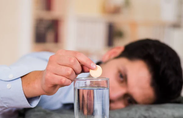 Stilig uttråkad man håller ett piller brustablett i handen redo att släppa i ett glas vatten — Stockfoto