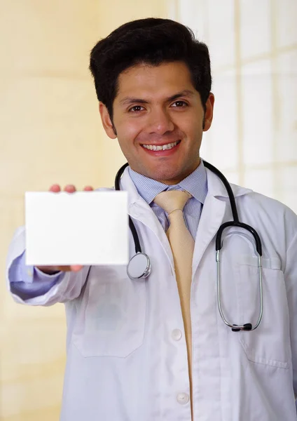 Уверенный в себе красивый улыбающийся доктор позирует и смотрит в камеру со стетоскопом на шее, указывая ему на медицинский рецепт — стоковое фото
