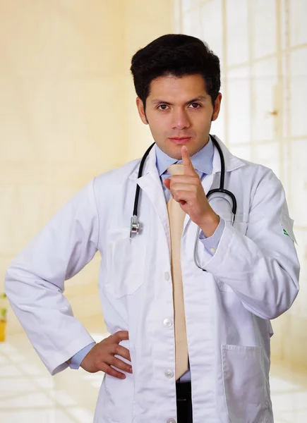 Sexy médico posando y mirando a la cámara con un estetoscopio alrededor de su cuello, en el fondo de la oficina — Foto de Stock