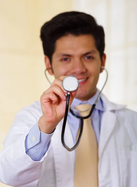 Zbliżenie na pewność przystojny Doktor uśmiechający się za pomocą stetoskopu, w tle office — Zdjęcie stockowe
