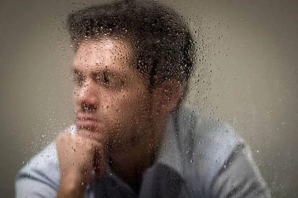 Жахливий молодий чоловік, за розмитим вікном з краплями, сірий фон — стокове фото