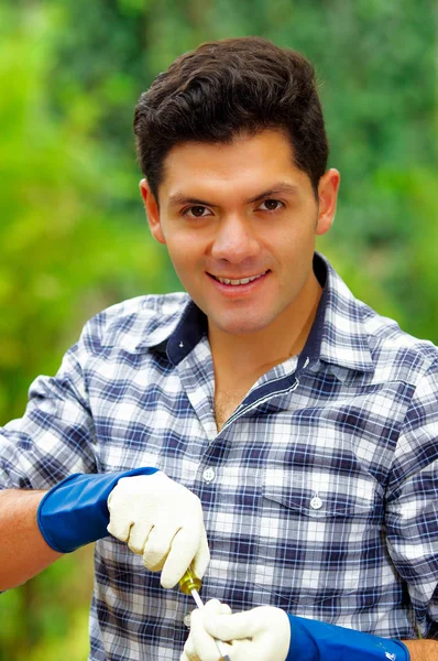 Atractivo joven constructor sonriente sosteniendo un destornillador con guantes de trabajo — Foto de Stock