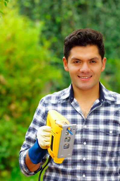 Close up of a man wearing job gloves working wood with electric jigsaw — Stock Photo, Image