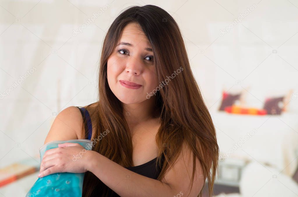 Close up of a beautiful woman holding ice gel pack on her arm, medical concept, in office background