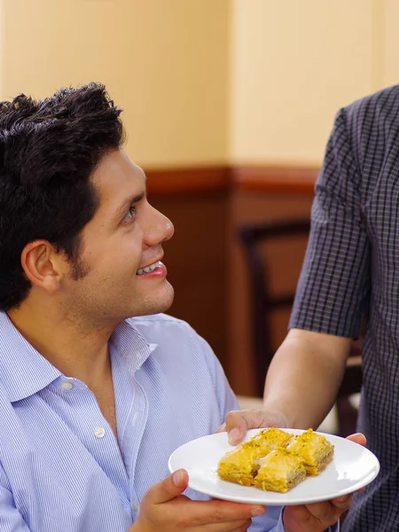 Hombre guapo sosteniendo un plato de deliciosa comida tradicional turca baklava con pistacho en un plato blanco —  Fotos de Stock