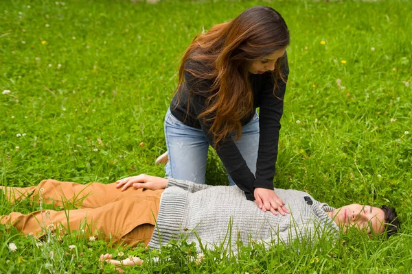 Krásná žena dávat první pomoc na pohledný mladý muž, kardiopulmonální resuscitace, v pozadí trávy — Stock fotografie