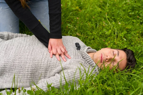 Mulher bonita dando primeiros socorros a um jovem bonito, ressuscitação cardiopulmonar, em um fundo de grama — Fotografia de Stock