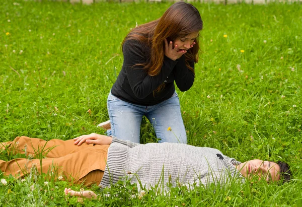 Surprised beautiful woman watching a handsome young man that is over a grass, cardiopulmonary resuscitation concept, in a grass background — Stock Photo, Image