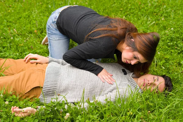 Молодая красивая женщина проверяет красивого молодого человека, если он еще дышит, концепция сердечно-легочной реанимации, на фоне травы — стоковое фото