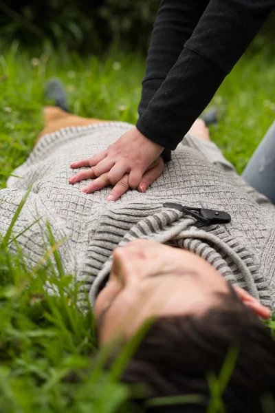 Close up of a beautiful woman giving first aid to a handsome young man, cardiopulmonary resuscitation, in a grass background — Stock Photo, Image