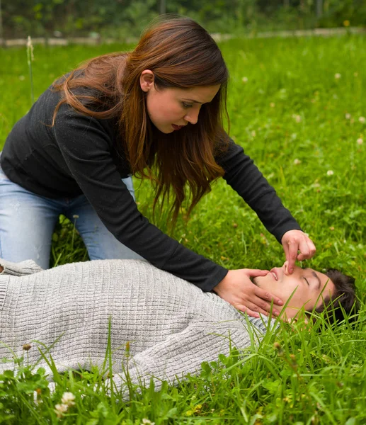 Vacker kvinna att ge fisrt stöd till en stilig ung man, hjärt-lungräddning, i gräs bakgrund — Stockfoto