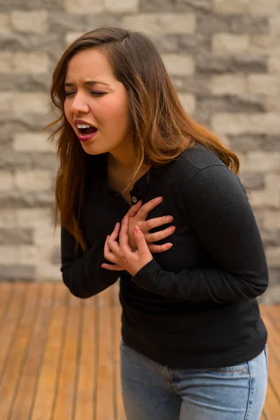 Mulher bonita jovem sentindo-se mal e agarrando seu peito, conceito de ressuscitação cardiopulmonar, em um fundo turvo — Fotografia de Stock