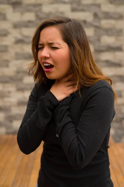 Joven hermosa mujer sintiéndose mal y agarrando su cuello, concepto de reanimación cardiopulmonar, en un fondo borroso —  Fotos de Stock