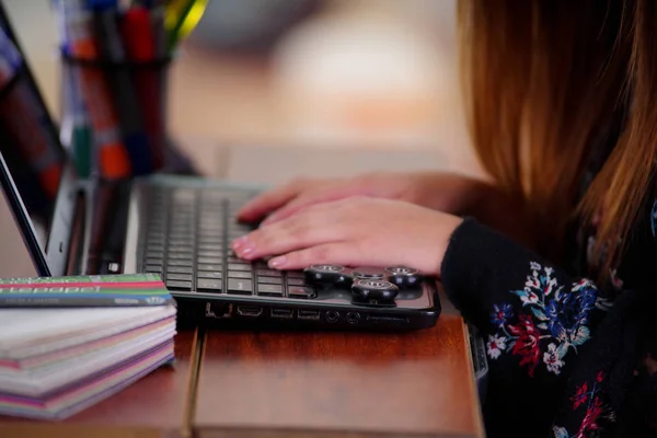 在计算机和流行坐立不安微调框玩具在笔记本电脑上办公室背景工作的年轻女子 — 图库照片