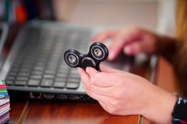 Ung kvinna håller en populära fidget spinner leksak i handen medan hon arbetar i sin dator på kontoret bakgrund — Stockfoto